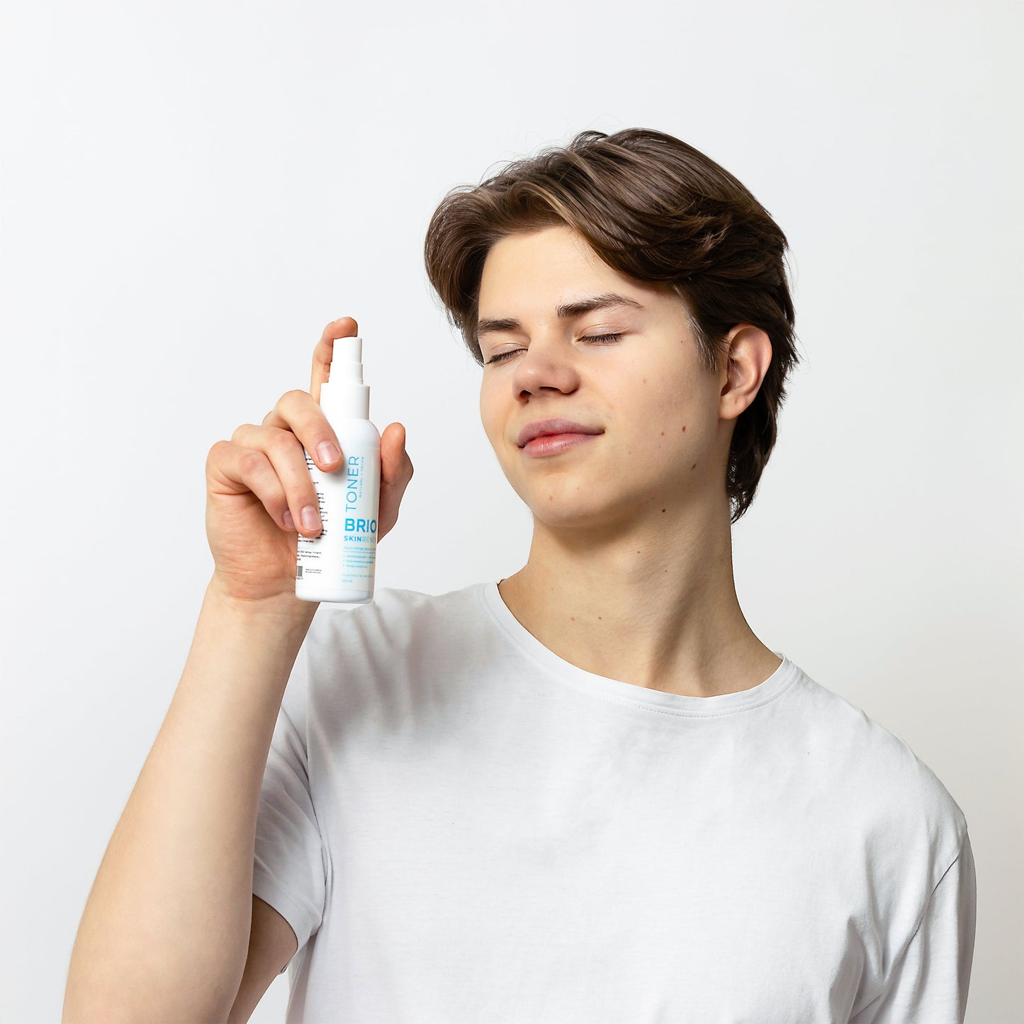 Youn man spraying Skin Renew toner on his skin. His eyes are closed and expression is calm.