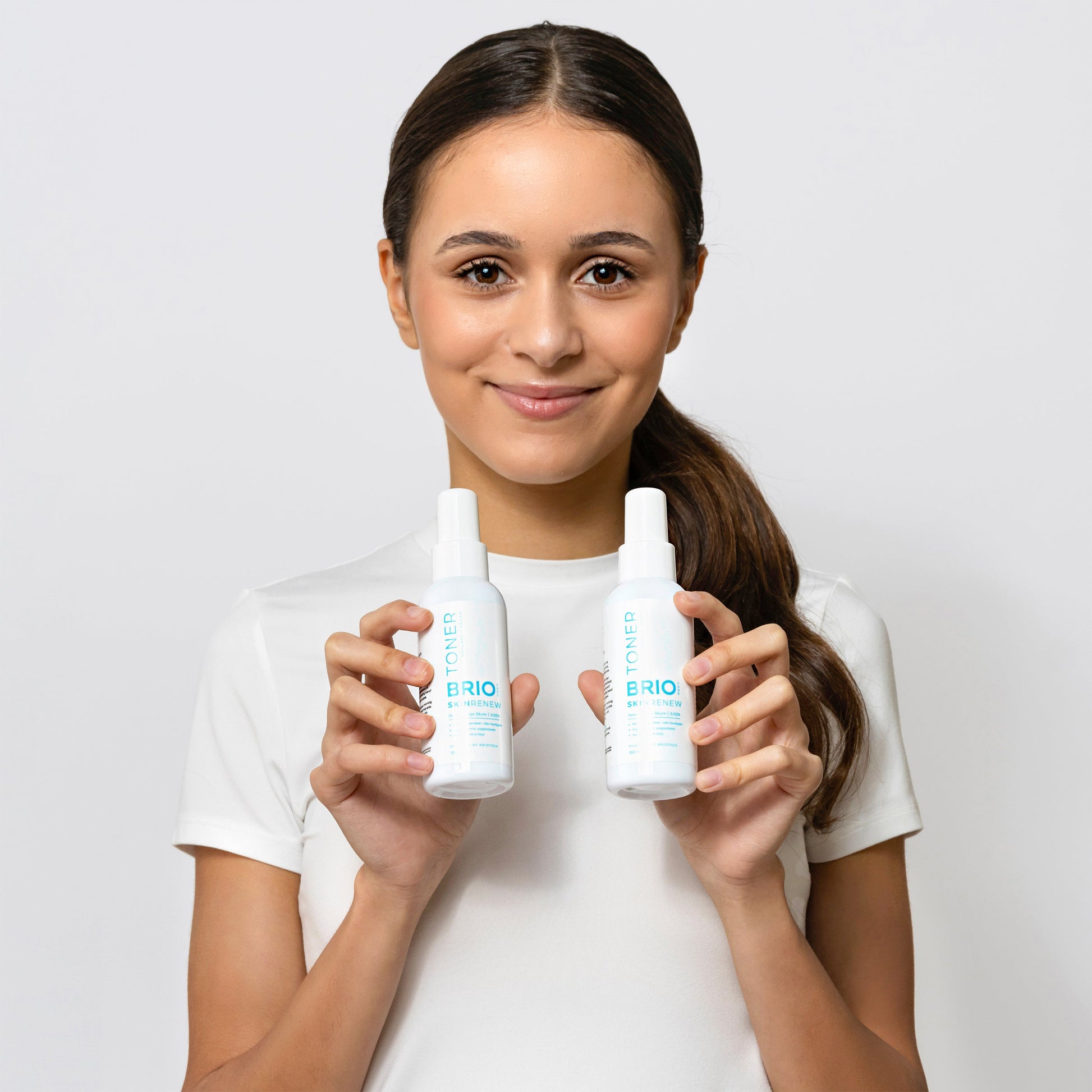 Young woman is holding two Skin Renew Toner bottles, smiling and looking directly to camera with opened eyes. Skin Renew Toner is dermatologically and clinically tested.